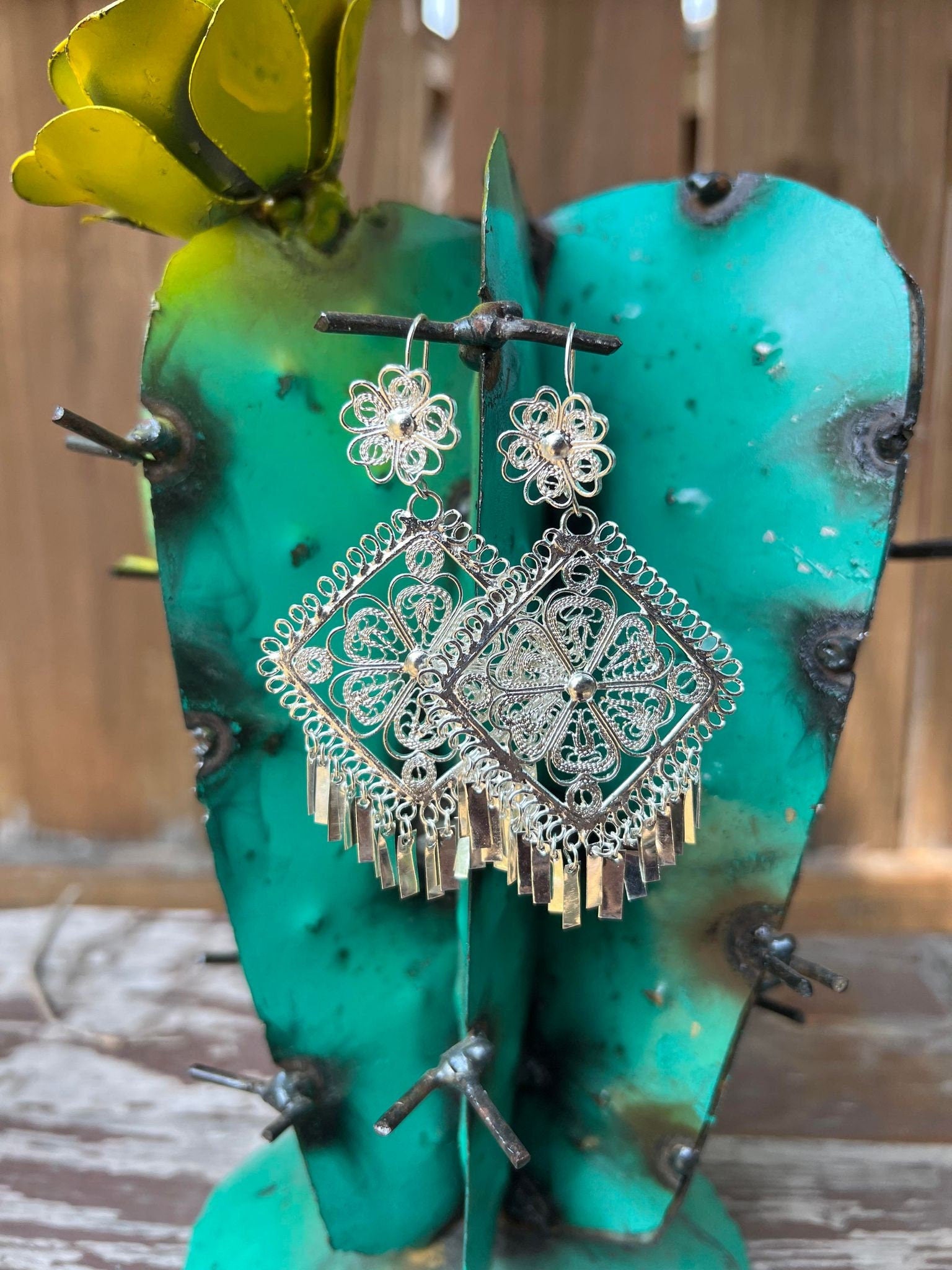 Filigree Silver Earrings Shaped like a triangle.  Near the earring hook there is a flower design. The middle is an intricate triangle containing a flower in the middle. Towards the bottom of the earring there are individual filigree columns dangling.