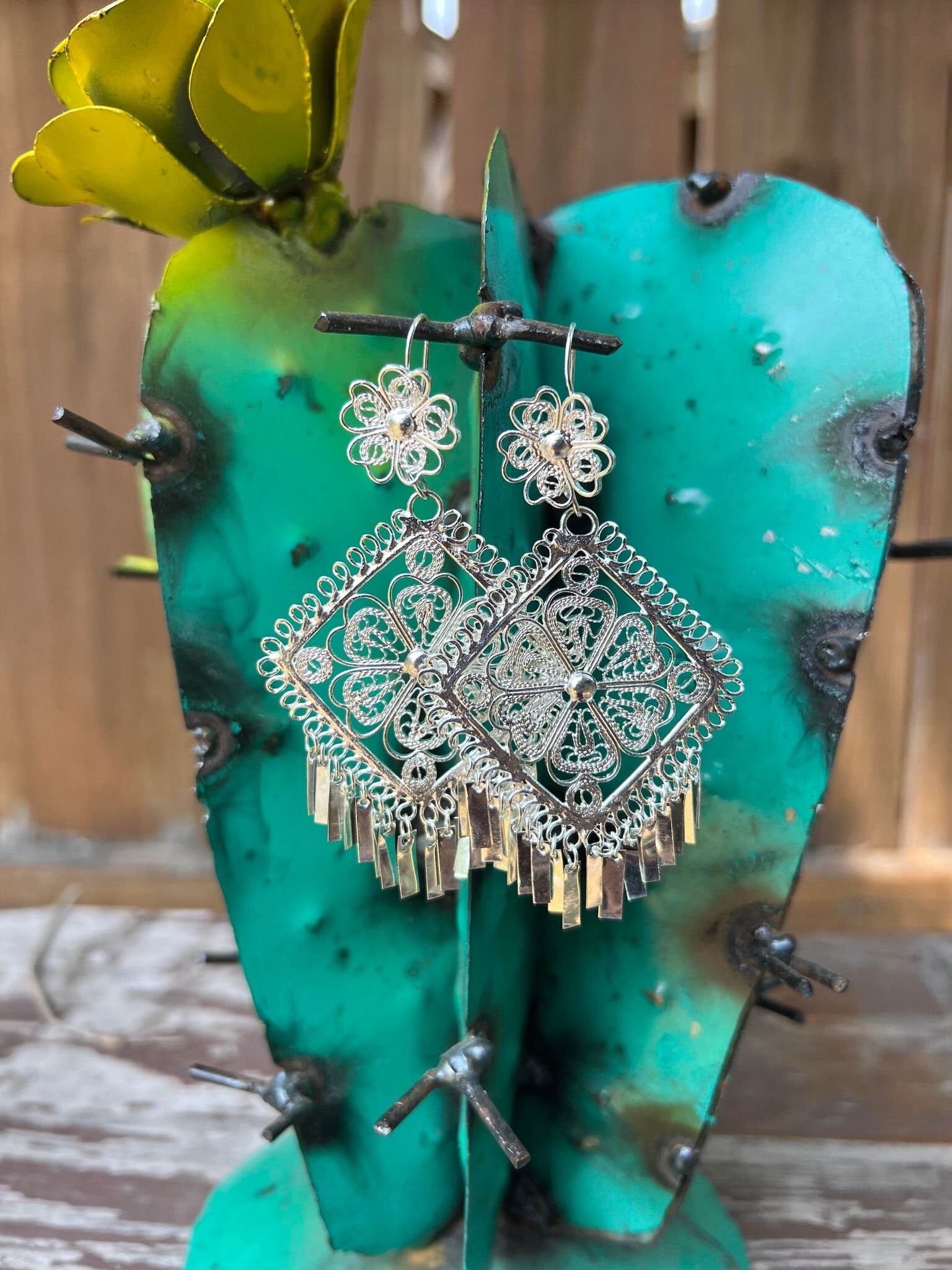 Image of Filigree Silver Earrings Shaped like a triangle.  Near the earring hook there is a flower design. The middle is an intricate triangle containing a flower in the middle. Towards the bottom of the earring there are individual filigree columns dangling.