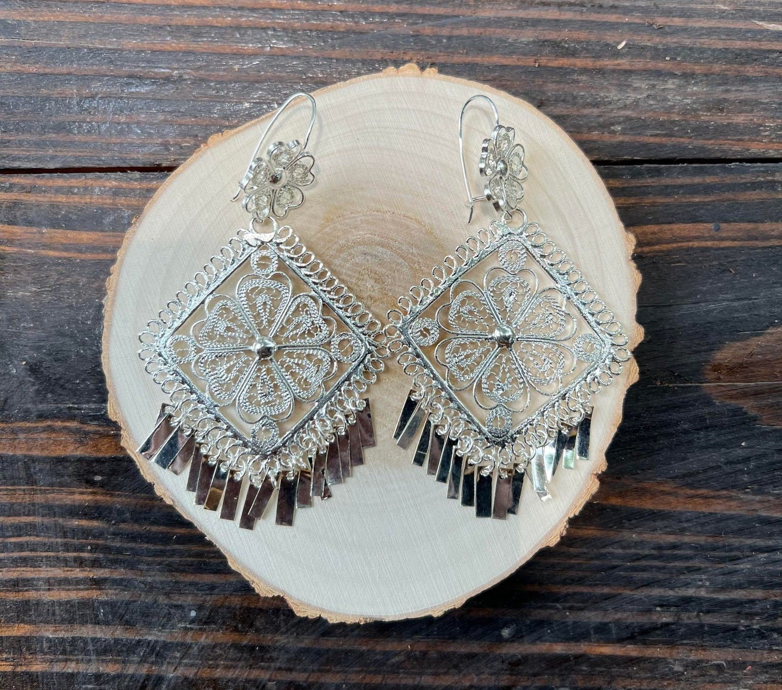 Silver Filigree Earrings on wooden circle. A close-up photo to see the intricate design of these artisan made earrings.