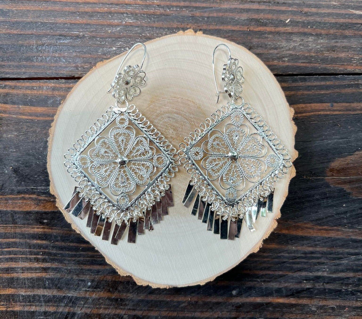 Image of Silver Filigree Earrings on wooden circle. A close-up photo to see the intricate design of these artisan made earrings.