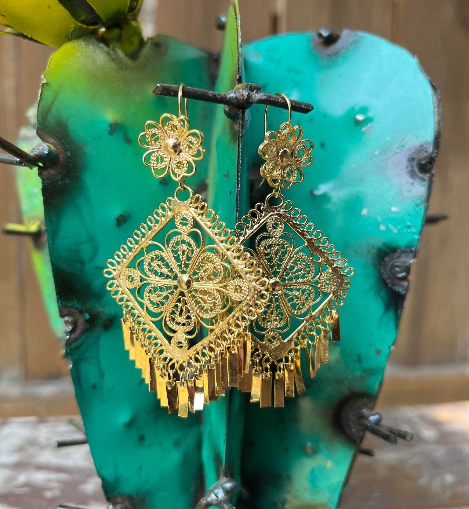 Image of Filigree Gold Earrings Shaped like a triangle.  Near the earring hook there is a flower design. The middle is an intricate triangle containing a flower in the middle. Towards the bottom of the earring there are individual filigree columns dangling.