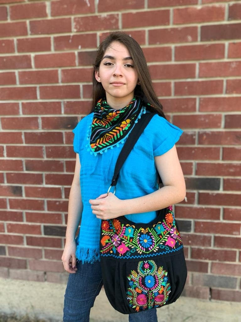 May include: A black embroidered tote bag with colorful floral designs. The bag has a black strap and a silver ring on the strap.