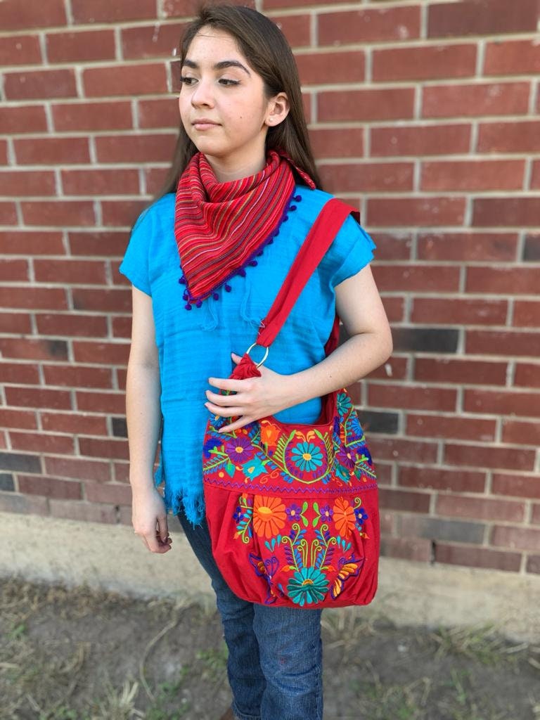 Image of May include: A red embroidered tote bag with colorful flowers and green leaves. The bag has a red strap and a silver ring on the strap.